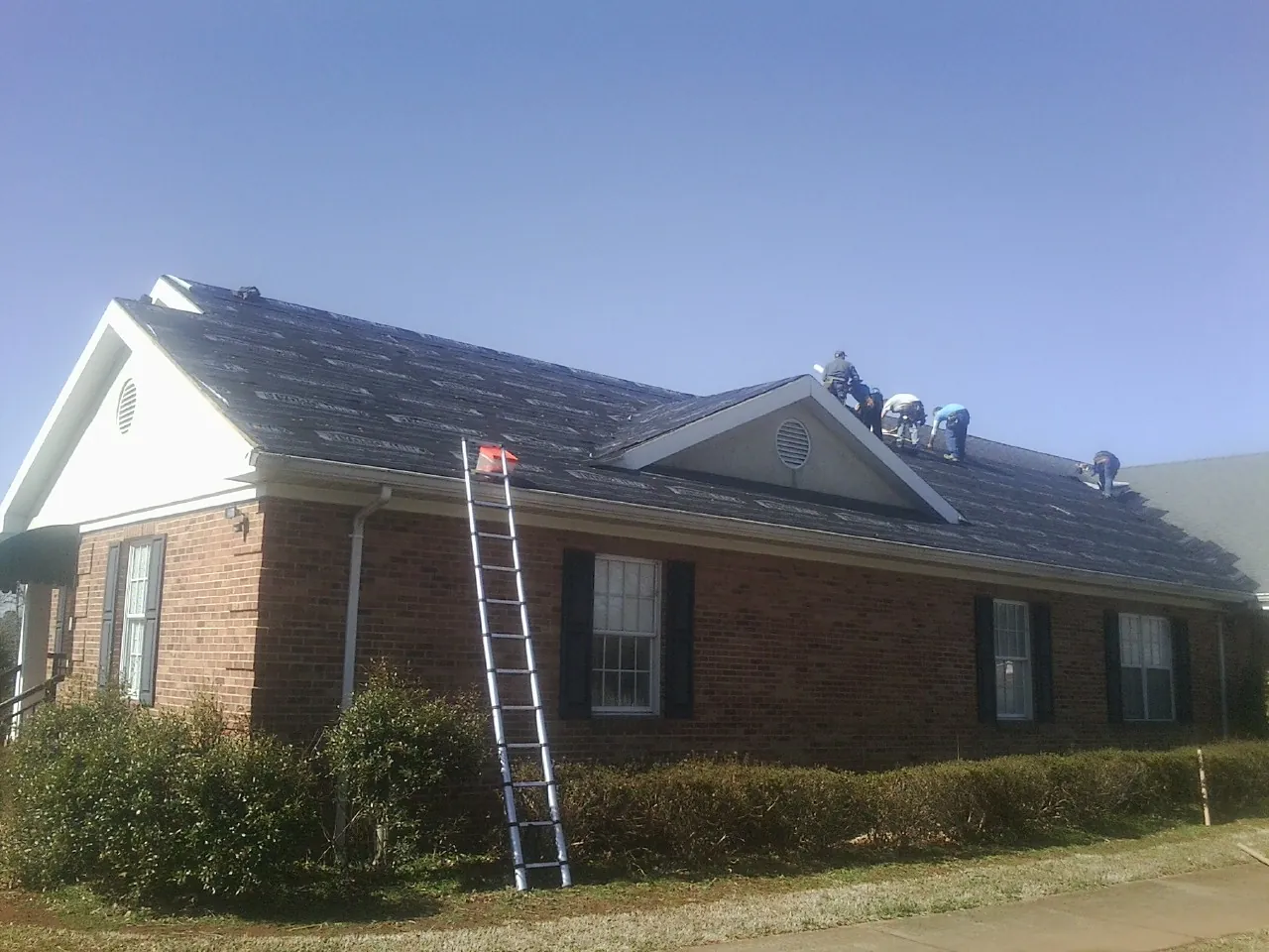 Crew tearing shingles off a brick ranch roof with a ladder set — Metal Roof Repair work by our crew in North Oxford