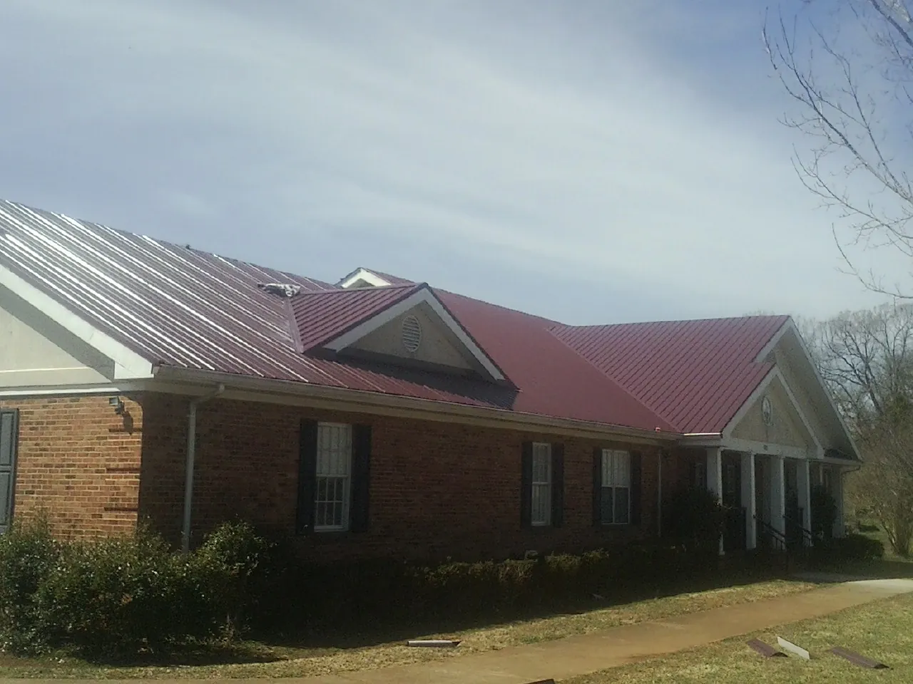 Red metal roof with gabled entries on a long brick building, from a Hail Damage Roof Repair job in North Oxford