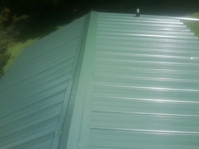 New green metal panels meeting at the ridge of a roof — Flat Roof Repair work by our crew in North Oxford