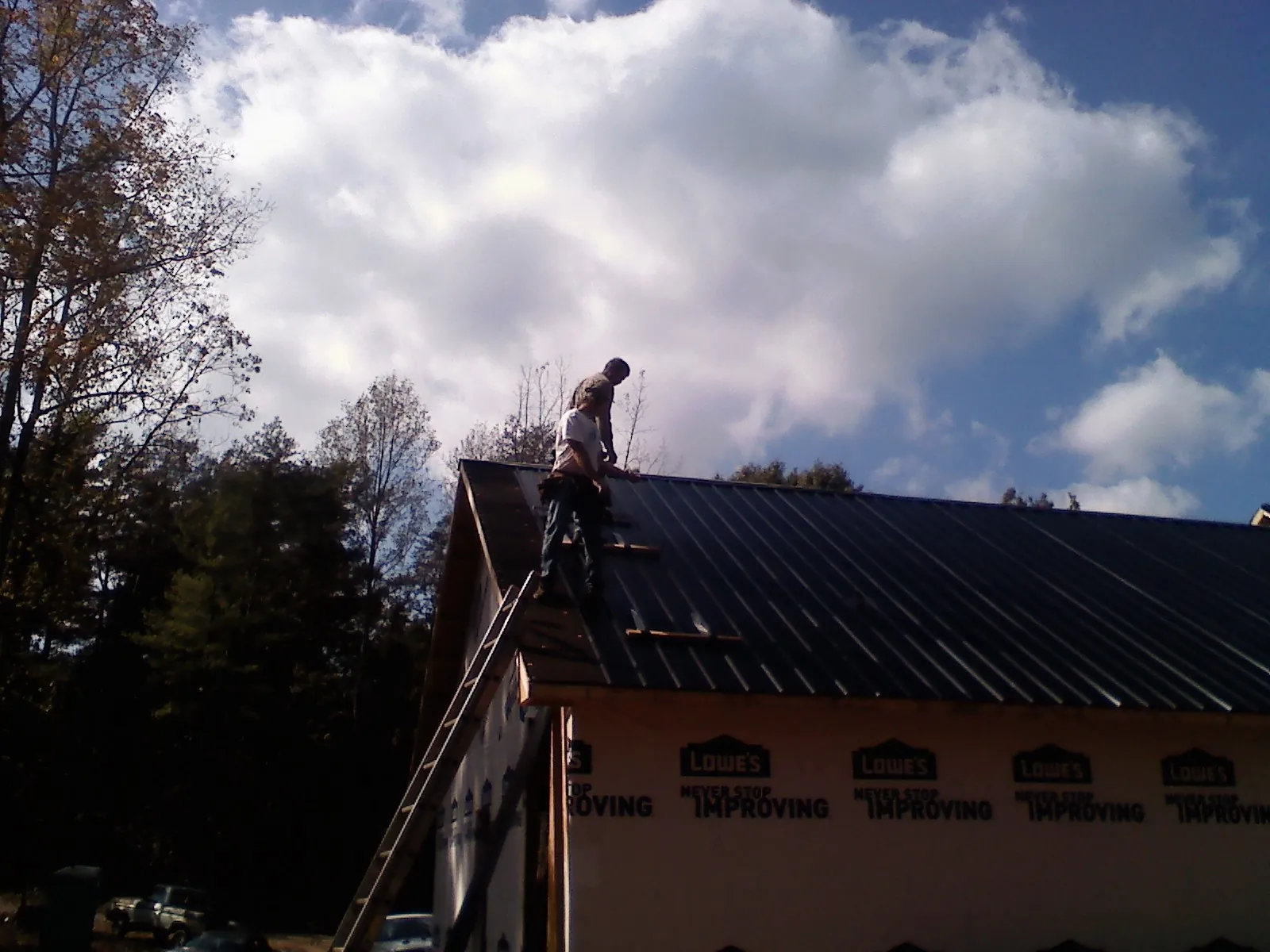 Roofer fastening dark metal panels high against a cloudy sky, from a Roof Inspection job in North Oxford