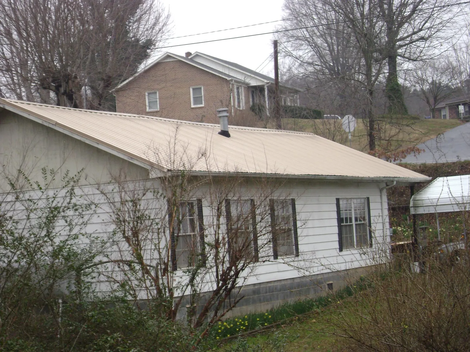 Tan metal roof on a white sided house set into a hillside — Commercial Roofing by Roofing Brothers in North Oxford